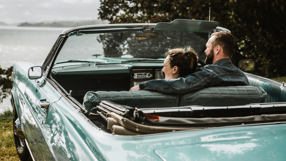 A couple relaxing together in their classic convertible beside the water