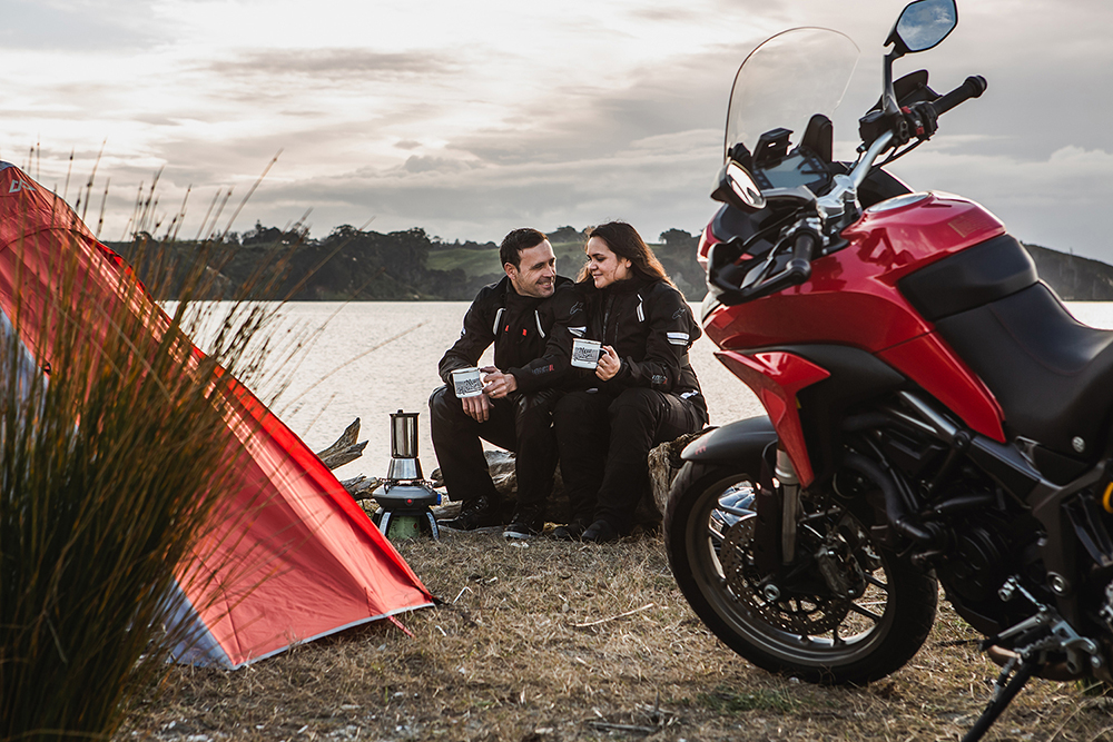Two motorcyclists sharing a drink beside their touring motorcycle and tent